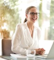 A cheerful lady dressed in white siting in front of a laptop