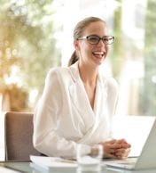 A cheerful lady dressed in white siting in front of a laptop