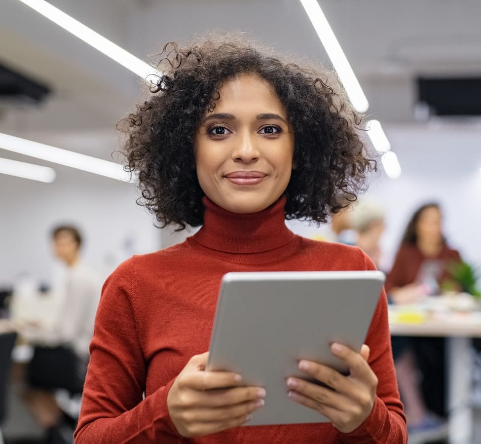 A woman smiling holding a tablet in an office